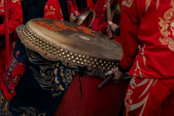 Don · 5928 x 3952 Cette photographie met en scène un tambour traditionnel richement décoré, sujet principal. La composition montre des motifs complexes et des perles incrustées, avec des détails de motifs floraux et animaux.Le cadrage est serré, centré sur l'instrument, avec une partie d’un vêtement rouge et or en arrière-plan. La lumière semble douce et naturelle, mettant en valeur les textures et les couleurs.Les couleurs dominantes sont le rouge, l’or et le noir, créant une ambiance chaleureuse et festive. Le style évoque l’artisanat traditionnel et culturel, évoquant une ambiance rituelle ou festive.