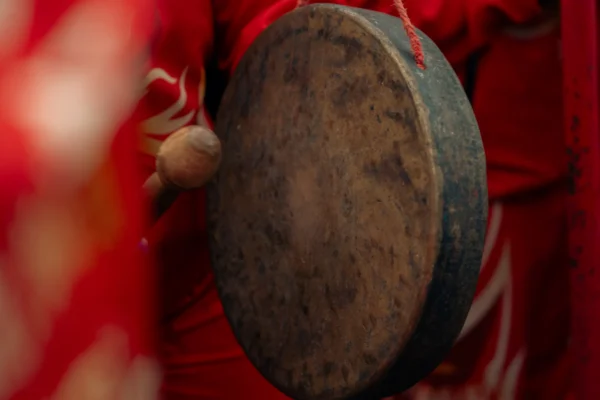 Don · 6173 x 4115 Cette photographie met en scène un tambour traditionnel comme sujet principal, probablement un gong ou un tambour de type tibétain. Le cadrage est serré, centré sur l’instrument, avec une partie des mains et des vêtements rouges en arrière-plan.La lumière est douce, créant des ombres subtiles. Les couleurs dominantes sont le rouge vif des vêtements et le brun-gris du tambour. Le style est documentaire et artistique, évoquant une ambiance culturelle et spirituelle, renforcée par les teintes chaudes et l’aspect rituel suggéré.