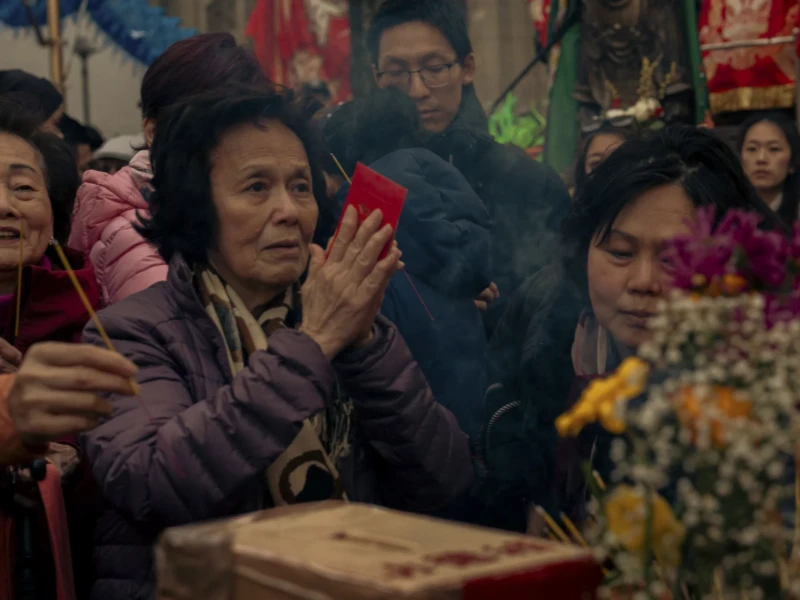 Nouvel an chinois Cette photographie capture un groupe de personnes, dont une femme âgée en costume traditionnel violet, comme sujet principal. La composition montre une scène dense et animée, avec des visages proches et des couleurs vives.Le cadrage est serré, mettant en valeur les expressions et les détails des vêtements. La lumière semble naturelle et tamisée, créant une ambiance chaleureuse et intime. Les couleurs dominantes sont les tons chauds (violet, rouge, orange) et les teintes pastel, typiques d’un environnement festif ou culturel.Le style évoque une ambiance traditionnelle et folklorique, renforcée par les accessoires et les expressions des participants.