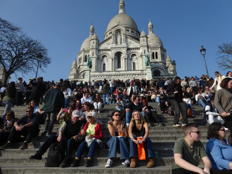 Christelle · 21/03/2026 · 4000 x 3000 Cette photographie montre le **Sacré-Cœur de Montmartre** à Paris, avec sa basilique blanche et sa coupole bleue. Le **sujet principal** est la foule assise sur les marches, en plein air. La **composition** est dynamique, avec un premier plan occupé par les personnes et un arrière-plan monumental.Le **cadrage** est large, capturant à la fois les visiteurs et l’architecture. La **lumière** est naturelle et claire, suggérant un jour ensoleillé. Les **couleurs dominantes** sont les tons pastel de la basilique (blanc, bleu) et les vêtements colorés des gens.Le style est **documentaire et touristique**, évoquant une **ambiance conviviale et paisible**, typique d’un lieu emblématique et fréquenté.