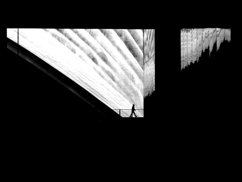 Cette photographie présente un sujet abstrait et géométrique. Le cadrage met en avant des formes en perspective, évoquant des structures architecturales ou des plis de tissu.La composition repose sur des lignes diagonales et des dégradés de blanc et de gris, créant une impression de profondeur. La lumière semble douce et uniforme, sans source apparente, renforçant l’aspect minimaliste.Les couleurs dominantes sont le blanc et le gris, dans une ambiance épurée et presque monochrome. Le style rappelle l’art abstrait ou une étude visuelle expérimentale, évoquant une sensation de mouvement et de fluidité malgré l’absence de détails concrets.