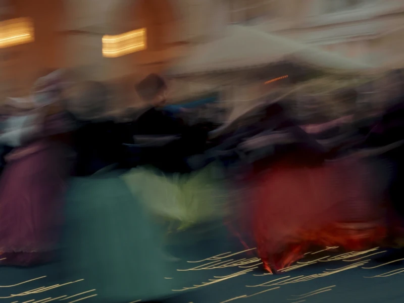 Cette photographie semble capturer un mouvement flou, probablement dû à une vitesse d'obturation lente. Le sujet principal est indistinct, suggérant une scène de foule ou de passage rapide.La composition est dynamique, avec des formes colorées et des contours flous. Le cadrage est serré, centré sur les éléments en mouvement. Les couleurs dominantes sont des teintes vives et contrastées : rouge, bleu, violet et vert.Le style est artistique et expérimental, évoquant une ambiance énergique et presque abstraite. La lumière semble naturelle mais diffuse, renforçant l'effet de mouvement et de flou.