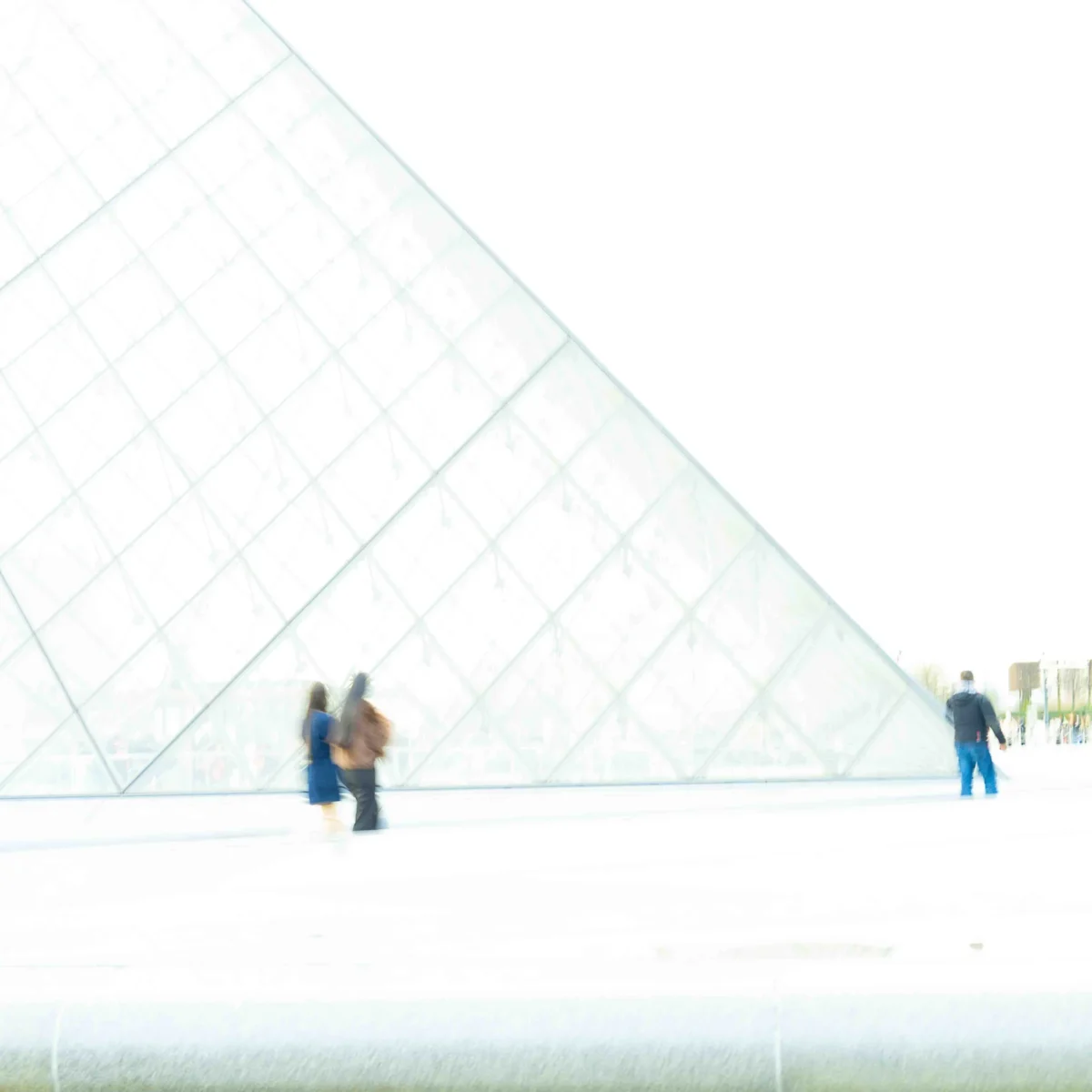 Jean-Paul · 19/12/2025 · 4280 x 4280 Cette photographie met en scène le **Pyramide du Louvre**, sujet principal. La composition est épurée, avec un cadrage serré sur la structure géométrique et ses reflets. Les trois silhouettes floues ajoutent une touche d'échelle humaine.La lumière est douce et diffuse, créant une ambiance légèrement blafarde. Les couleurs dominantes sont des **teintes grises et blanches**, renforcées par un flou artistique. Le style, sobre et minimaliste, évoque une atmosphère moderne et contemplative, presque onirique. L'image suggère une visite culturelle dans un cadre architectural emblématique.