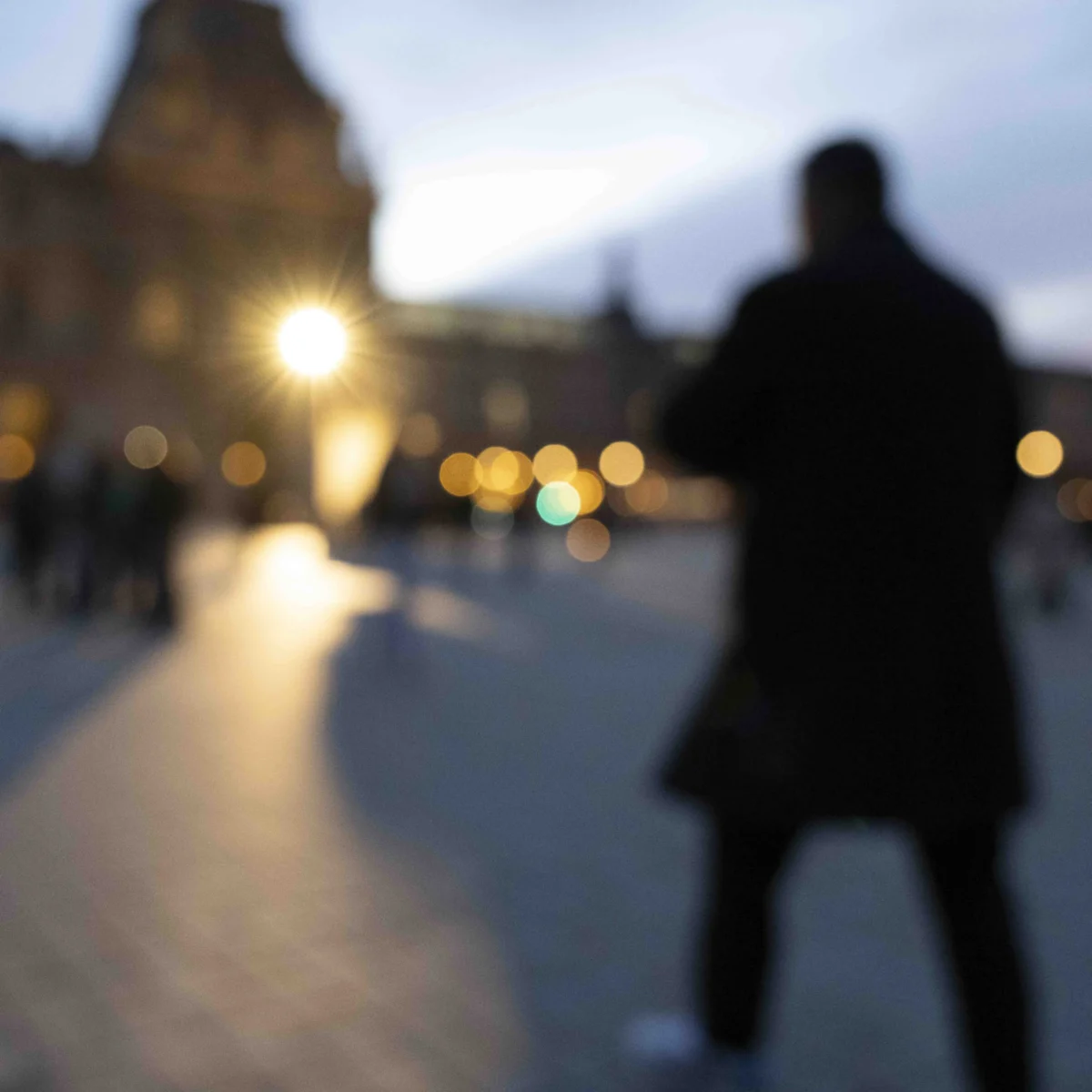 Jean-Paul · 19/12/2025 · 5501 x 5501 Cette photographie met en scène un **sujet principal flou**, une silhouette humaine de dos, vêtue d’un manteau sombre. La **composition** joue sur le contraste entre le premier plan net et l’arrière-plan flou, créant une impression de profondeur.Le **cadrage** est serré sur la silhouette, avec une légère inclinaison. La **lumière**, douce et tamisée, provient probablement des lampadaires, éclairant faiblement la scène. Les **couleurs dominantes** sont des tons froids (bleutés) et chauds (jaunes des lumières).Le style est **minimaliste et abstrait**, évoquant une **ambiance nocturne et mélancolique**, presque onirique.
