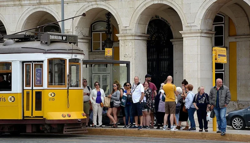 Pascale · 12/06/2018 · 1000 x 571 Cette photographie montre un tramway jaune traditionnel, sujet principal, typique des villes comme Lisbonne. La composition met en scène des passagers attendant ou descendant, encadrés par une architecture coloniale avec des arcs et des portes en bois.Le cadrage est serré sur le tramway et les personnes, capturant une scène dynamique. La lumière est naturelle et douce, suggérant un jour ensoleillé. Les couleurs dominantes sont le jaune vif du tramway, les tons neutres des bâtiments et les vêtements colorés des gens.Le style est documentaire et réaliste, évoquant une ambiance urbaine animée et chaleureuse.