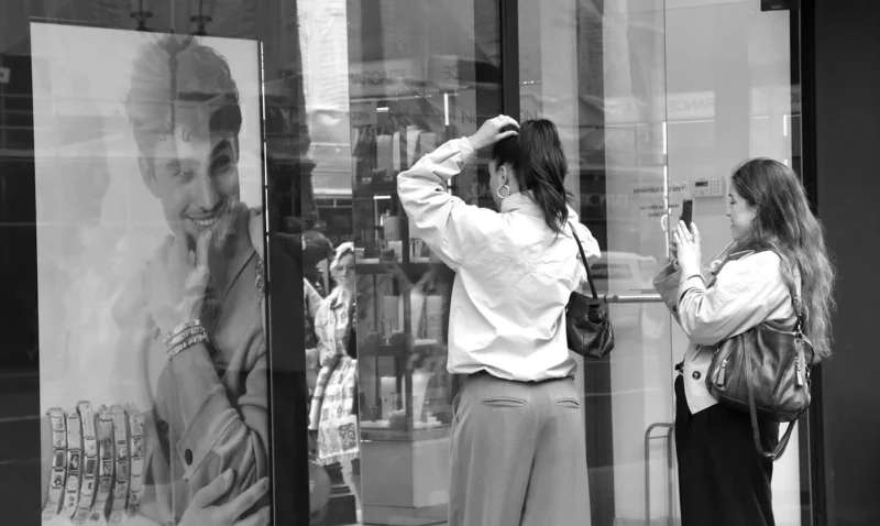 Franck T. · 08/03/2026 · 1400 x 837 Cette photographie en noir et blanc montre deux femmes observant une œuvre d’art abstraite ou pixelisée représentant un visage masculin. La composition met en valeur le contraste entre les deux personnages et l’art mural.Le cadrage est serré sur les femmes et l’œuvre, créant une ambiance intimiste. La lumière semble naturelle et douce, éclairant les sujets sans ombres marquées. Les couleurs, réduites au noir et blanc, accentuent les textures et les contrastes. Le style est sobre et moderne, évoquant une réflexion artistique et contemplative. L’ambiance est calme et analytique.