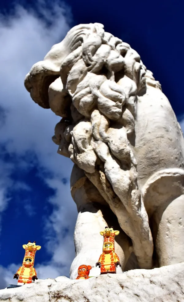 Franck TREBOIT · 14/03/2026 · 851 x 1400 Cette photographie met en scène une **sphinge en pierre** comme sujet principal, avec deux petites figurines dorées (probablement des lions) placées devant elle. La **composition** joue sur le contraste entre le monument imposant et les figurines minuscules.Le **cadrage** est serré sur la tête de la sphinge, avec un ciel bleu clair en arrière-plan. La **lumière** naturelle, vive et contrastée, accentue les textures et les ombres. Les **couleurs dominantes** sont les tons gris-beige de la pierre, le bleu du ciel et les dorés des figurines.Le style est **symbolique et dramatique**, créant une ambiance de **mystère et de grandeur**.