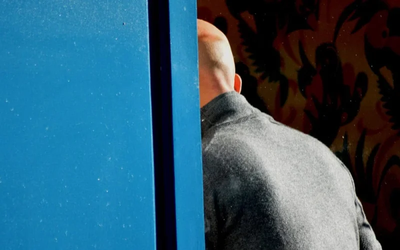 Franck T. · 17/11/2018 · 1000 x 624 Cette photographie met en scène un homme vu de dos, partiellement caché derrière un cadre bleu. Le sujet principal est son profil flou et son manteau gris.La composition joue sur le contraste entre le cadre bleu vif et le fond coloré et texturé. Le cadrage serré isole le sujet, créant une ambiance mystérieuse.La lumière semble naturelle et douce, éclairant légèrement le visage et le manteau. Les couleurs dominantes sont le bleu intense du cadre et les tons chauds du fond.Le style est épuré et minimaliste, évoquant une ambiance contemplative et introspective.