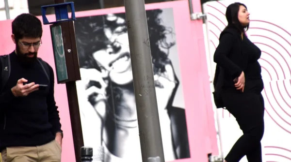 Franck TREBOIT · 07/03/2026 · 1400 x 782 Cette photographie montre deux personnes en arrière-plan flou, suggérant un mouvement urbain. Le sujet principal semble être une affiche murale stylisée, en noir et blanc, représentant une silhouette féminine stylisée.La composition joue sur les contrastes entre les éléments nets (l’affiche) et flous (les passants). Le cadrage est serré sur l’affiche, avec une lumière naturelle douce. Les couleurs dominantes sont le rose vif du mur et les tons neutres de l’affiche.Le style est épuré et moderne, évoquant une ambiance contemporaine et artistique dans un cadre urbain animé.