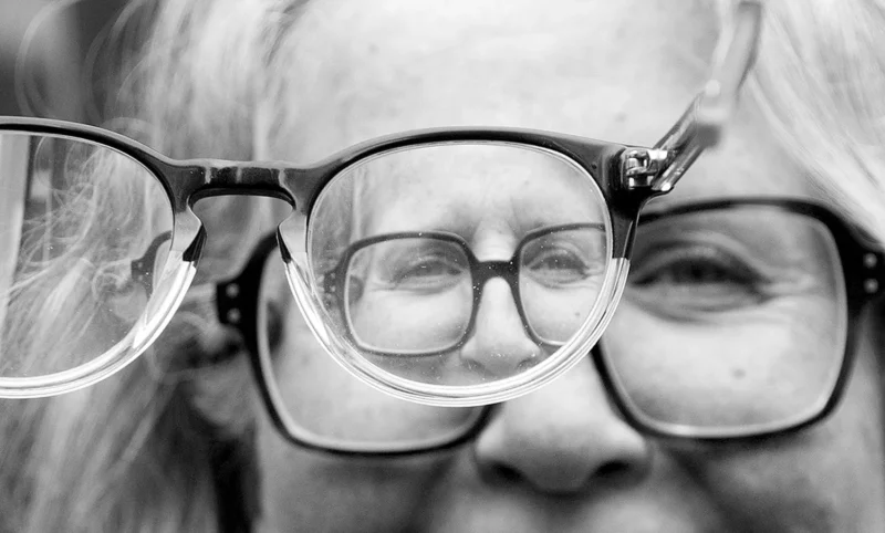 Pascale · 11/04/2026 · 1500 x 903 Cette photographie met en scène un visage flou d’une personne âgée, partiellement caché par une paire de lunettes posées devant ses yeux. Le sujet principal est ces lunettes, qui encadrent le regard et créent un jeu de superposition.Le cadrage est serré, centré sur les yeux et les lunettes. La lumière est douce, avec des contrastes modérés, accentuant les textures et les détails des lunettes. Les couleurs dominantes sont les tons de gris, typiques d’une photo en noir et blanc, renforçant une ambiance intemporelle et mélancolique. Le style est épuré et artistique, évoquant une réflexion sur le temps et la perception.