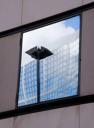 Pascale · 28/03/2026 · 1027 x 1400 Cette photographie montre un reflet dans une vitre. Le sujet principal est une structure métallique en forme de pyramide tronquée, reflétée dans une fenêtre. La composition joue sur la symétrie et la répétition des reflets des bâtiments modernes en arrière-plan.Le cadrage est serré, centré sur la structure et la vitre. La lumière est naturelle, avec des contrastes doux entre les ombres et les zones éclairées. Les couleurs dominantes sont les teintes grises et bleutées des bâtiments, avec des touches de blanc et de noir.L’ambiance est urbaine et contemporaine, mettant en valeur l’architecture moderne et les jeux de lumière.