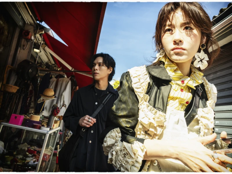 Thierry · 25/04/2026 · 3840 x 2560 Cette photographie met en scène deux jeunes femmes en extérieur. La personne au premier plan, vêtue d’un manteau clair et d’un foulard, semble être le sujet principal, avec un regard intense et une posture légèrement penchée. L’autre femme, en arrière-plan, est partiellement visible et semble marcher.La composition est dynamique, avec un cadrage serré sur les visages et une profondeur de champ réduite. La lumière est naturelle, douce mais contrastée, créant des ombres marquées. Les couleurs dominantes sont des tons neutres (beige, gris) avec des touches de rouge et de bleu.L’ambiance est urbaine et légèrement mélancolique, évoquant une scène de rue authentique et moderne.