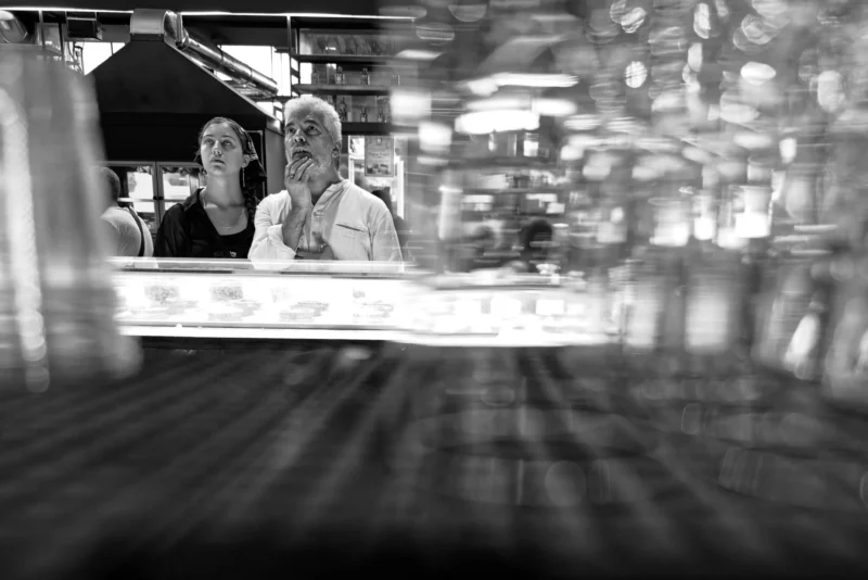 Mickaël · 2156 x 1439 Cette photographie en noir et blanc montre deux personnes assises dans un espace confiné, probablement un véhicule en mouvement. Le sujet principal semble être les deux individus, dont les visages sont floutés.La composition met en valeur leur interaction, avec un cadrage serré et une perspective légèrement inclinée. La lumière est douce mais contrastée, créant des ombres marquées. Les couleurs dominantes, bien sûr, sont les nuances de gris typiques du noir et blanc.Le style est documentaire et spontané, évoquant une ambiance intime et dynamique, renforcée par le flou de mouvement.