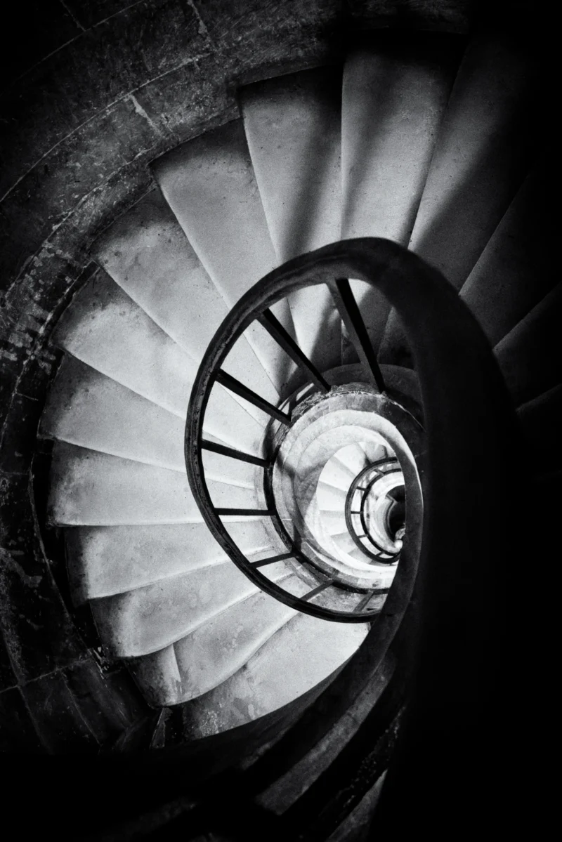Philippe · 08/11/2025 · 2668 x 4000 Cette photographie met en scène un **escalier en colimaçon** comme sujet principal. La **composition** repose sur une perspective descendante, créant une illusion de profondeur et de spirale infinie. Le **cadrage** est serré, centré sur les marches et la rampe métallique.La **lumière**, tamisée et contrastée, accentue les ombres et donne un aspect dramatique. Les **couleurs dominantes** sont les tons de gris, renforçant l’aspect monochrome et mystérieux.Le **style** est épuré et artistique, évoquant une **ambiance** à la fois hypnotique et angoissante, presque onirique.