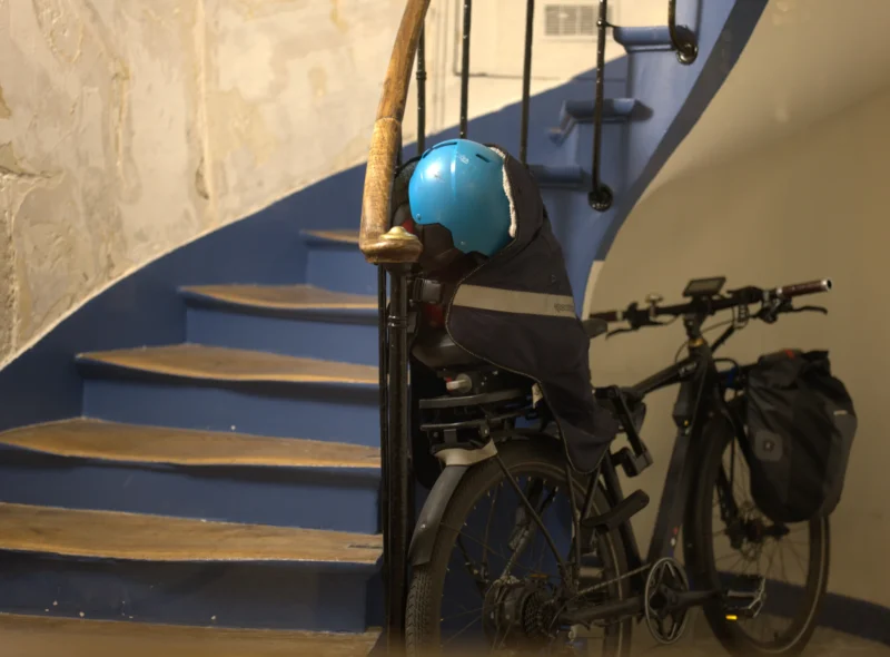 Bao · 5443 x 4016 Cette photographie montre deux vélos stationnés au pied d’un escalier en colimaçon. Le sujet principal est le vélo avant, équipé d’un porte-bagages portant un casque bleu.La composition est simple et symétrique, avec une mise en valeur des escaliers en arrière-plan. Le cadrage est serré, centré sur les vélos et l’escalier. La lumière est douce et naturelle, créant des ombres discrètes. Les couleurs dominantes sont les tons neutres (gris, beige) avec des touches bleues et noires.Le style est réaliste et sobre, évoquant une ambiance calme et urbaine.