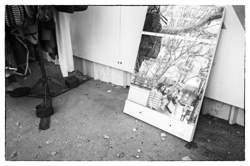 Thierry · 11/04/2026 · 3840 x 2560 Cette photographie en noir et blanc montre une grande toile ou affiche représentant un paysage hivernal, partiellement déchirée et posée contre un mur extérieur.Le cadrage inclut aussi un pied de caméra et des débris au sol. La composition est simple, avec un premier plan désordonné et un arrière-plan minimaliste. La lumière semble naturelle, mais contrastée, accentuant les textures et ombres.Les tons dominants sont les gris et noirs, renforçant une ambiance froide et mélancolique. Le style est documentaire, évoquant une scène abandonnée ou en cours de préparation artistique.