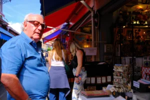 Dominique · 25/04/2026 · 7728 x 5152 Cette photographie montre un homme âgé en bleu comme sujet principal, observant un marché nocturne. La composition inclut des étals colorés en arrière-plan, avec des produits variés et des lumières chaudes.Le cadrage est serré sur l’homme, mais inclut aussi des personnes en arrière-plan. La lumière est douce et artificielle, créant une ambiance chaleureuse. Les couleurs dominantes sont des teintes vives (rouges, bleus) et des tons chauds (jaunes, oranges). Le style est documentaire et spontané, évoquant une scène de vie quotidienne animée et conviviale.