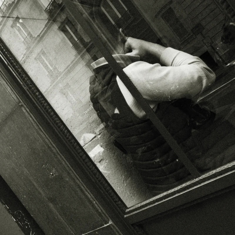Nathalie F. · 11/04/2026 · 4160 x 4160 Cette photographie en noir et blanc met en scène un sujet principal : une personne assise sur un rebord de fenêtre, les pieds pendants. La composition est dynamique, avec un cadrage serré qui accentue l’isolement et la vulnérabilité du personnage.La lumière est douce, créant des contrastes subtils et des ombres marquées. L’ambiance est mélancolique et introspective, renforcée par le style documentaire et l’absence de couleurs.Les tons gris et noirs dominent, soulignant une atmosphère à la fois poétique et légèrement angoissante.