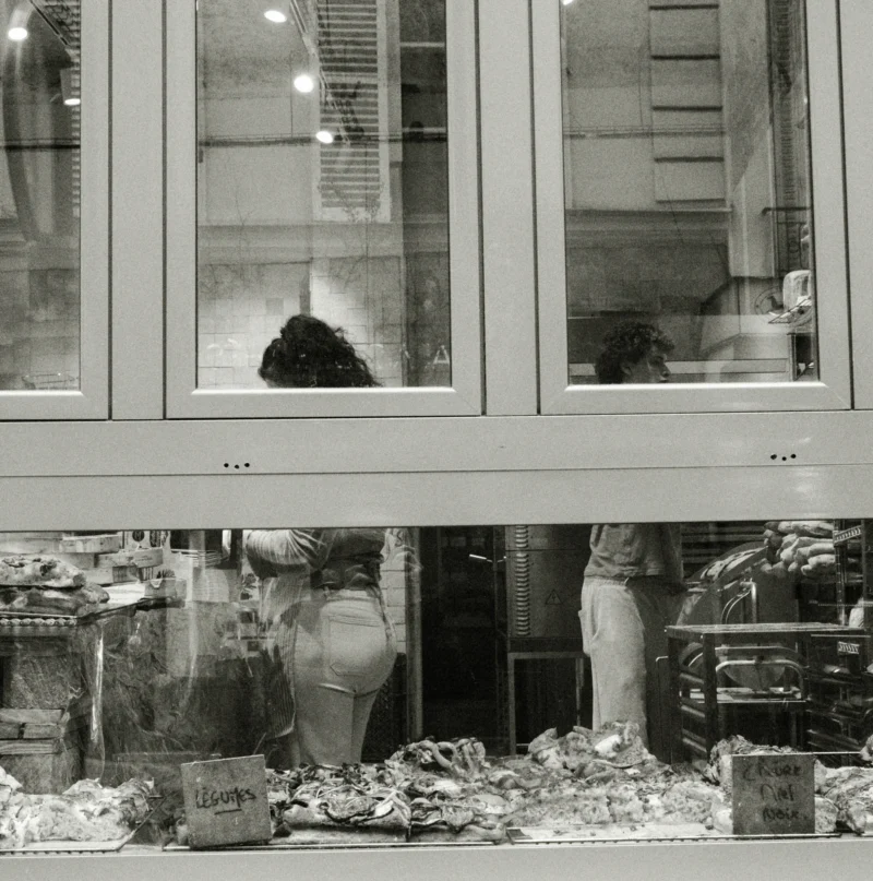 Nathalie F. · 11/04/2026 · 3726 x 3761 Cette photographie en noir et blanc montre une vitrine de magasin, probablement une boucherie ou une poissonnerie. Le sujet principal est l'arrangement de produits frais, comme des poissons et des viandes, disposés sur un comptoir.La composition est symétrique avec des portes vitrées reflétant l'intérieur du magasin. Le cadrage est serré, mettant en valeur les produits et les détails de la vitrine. La lumière est douce et naturelle, créant des contrastes subtils. Les couleurs dominantes sont les nuances de gris, typiques d'une photo en noir et blanc.Le style est réaliste et documentaire, évoquant une ambiance rétro et authentique.
