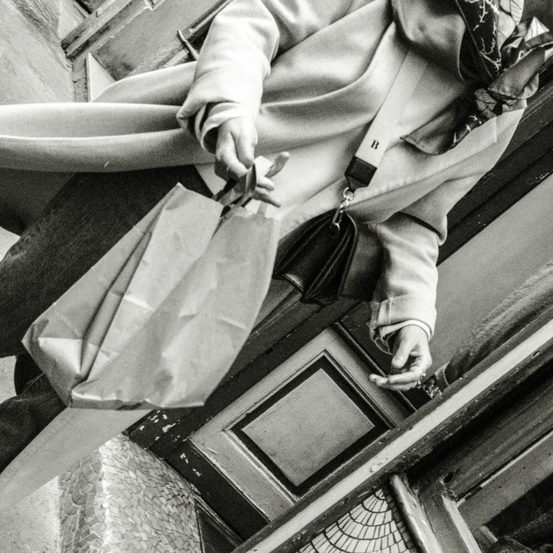 Nathalie F. · 11/04/2026 · 4160 x 4160 Cette photographie en noir et blanc met en scène une personne assise, probablement dans un lieu public comme un bus ou un train. Le sujet principal est ses jambes et ses pieds, avec une attention portée sur ses chaussures élégantes et ses sacs à main.La composition est serrée, centrée sur les détails des pieds et des accessoires. Le cadrage est bas, offrant une perspective originale. La lumière est douce, créant des contrastes subtils et des ombres marquées. Les couleurs dominantes, bien que monochromes, jouent sur les nuances de gris.Le style est documentaire et intime, évoquant une ambiance urbaine et contemporaine.