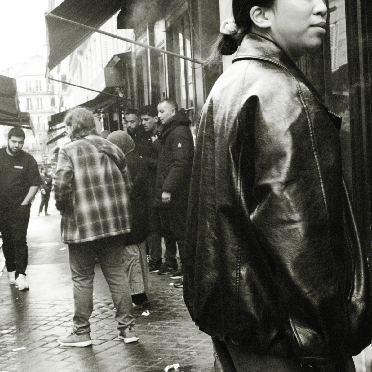 Nathalie F. · 11/04/2026 · 4160 x 4160 Cette photographie en noir et blanc met en scène un homme en veste de cuir comme sujet principal, vu de dos, marchant dans une rue animée. La composition montre une foule en arrière-plan, légèrement floue, créant un effet de profondeur.Le cadrage serré sur le sujet principal, avec une lumière naturelle diffuse, accentue les contrastes et les textures. Les couleurs dominantes, bien que monochromes, jouent sur les nuances de gris et de noir, renforçant l'atmosphère urbaine et légèrement mélancolique. Le style est documentaire, capturant un instant de vie quotidienne avec une touche d'intimité et de réalisme.