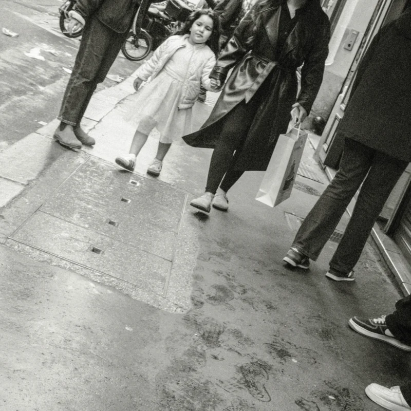 Nathalie F. · 4160 x 4160 Cette photographie en noir et blanc capture une scène urbaine anonyme. Le sujet principal semble être une femme vêtue d’un manteau clair, entourée de passants flous. La composition est dynamique, avec des jambes et pieds en mouvement, suggérant une foule en déplacement.Le cadrage est serré, centré sur les bas des personnes, créant une impression de densité et d’anonymat. La lumière est naturelle, probablement diffuse, sans ombres marquées. Les tons dominants sont les gris et noirs, typiques du noir et blanc, renforçant l’ambiance sobre et réaliste.Le style est documentaire, reflétant une instantanéité de la vie quotidienne, avec une ambiance urbaine et légèrement mélancolique.