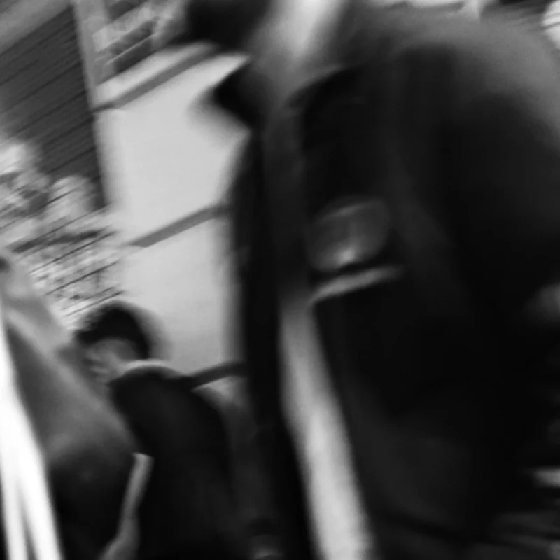 Nathalie F. · 23/04/2026 · 4160 x 4160 Cette photographie présente un sujet flou et peu identifiable, probablement une personne en mouvement. La composition est simple, avec un cadrage serré qui isole le visage et une partie du corps. La lumière est douce mais insuffisante, créant des contrastes faibles et une ambiance peu définie.Les couleurs dominantes sont les tons grisâtres, typiques d'une image en noir et blanc ou surexposée. Le style est minimaliste et brut, évoquant une impression de spontanéité ou de mouvement rapide. L'ambiance est mystérieuse et abstraite, renforcée par le flou et le manque de détails nets.