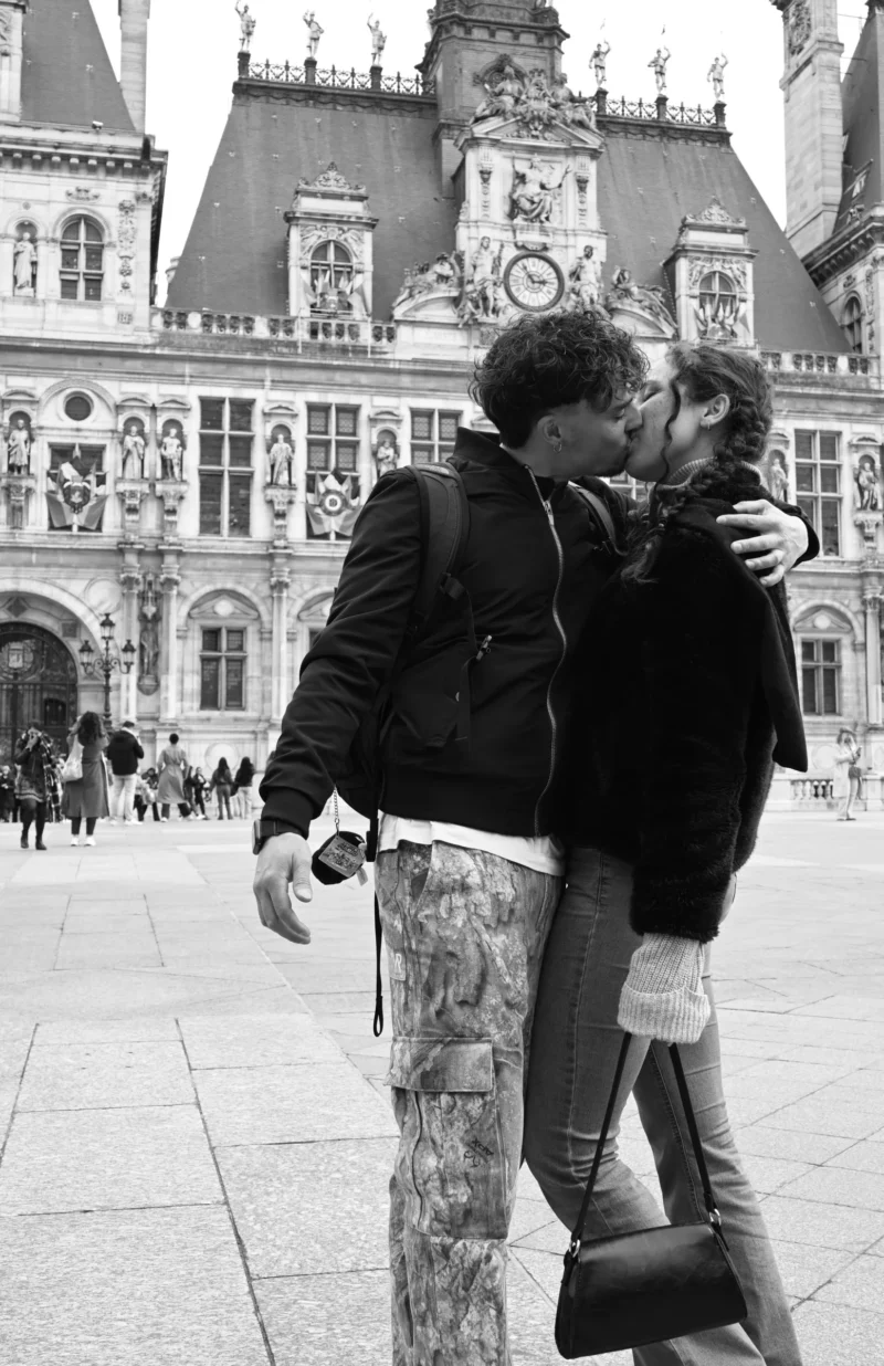 Aurélie · 15/01/2021 · 3234 x 4993 Cette photographie en noir et blanc met en scène un couple qui s'embrasse tendrement. Le sujet principal est centré sur eux, avec un cadrage serré qui isole leur intimité.L'arrière-plan montre un bâtiment architectural imposant, probablement une mairie ou un édifice historique. La lumière est naturelle, douce et légèrement diffuse, créant des contrastes subtils. L'absence de couleurs accentue les textures et les jeux d'ombres.L'ambiance est romantique et nostalgique, renforcée par le style vintage du cliché.