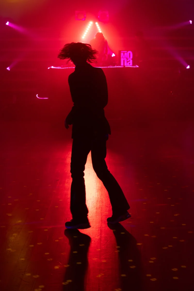 Daniel · 13/02/2025 · 2415 x 3622 Cette photographie met en scène un danseur en silhouette, sujet principal, en mouvement sur une piste. La composition est dynamique, avec un cadrage serré qui isole le danseur. La lumière, tamisée et directionnelle, crée des jeux d'ombres et de contrastes, accentuant l'atmosphère mystérieuse. Les couleurs dominantes sont les teintes rouges et violettes, renforçant une ambiance nocturne et sensuelle. Le style évoque une scène de club ou de spectacle, avec une touche artistique et cinématographique. L'ambiance est intense, presque théâtrale, mettant en valeur l'énergie et la grâce du danseur.