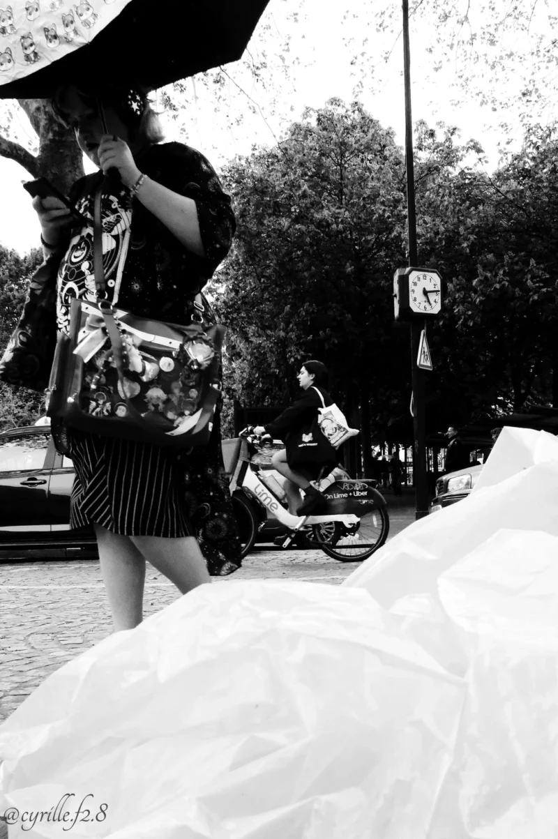 Cyrille · 11/04/2026 · 1347 x 2026 Cette photographie en noir et blanc met en scène une femme comme sujet principal, vêtue d’une robe à rayures et d’un chapeau, tenant un sac. La composition joue sur les contrastes avec des éléments urbains en arrière-plan (moto, trottoir, arbres).Le cadrage est serré sur ses jambes et sa robe, créant un effet de flou artistique. La lumière semble naturelle, douce mais contrastée, accentuant les ombres et les détails. Les couleurs, bien que monochromes, exploitent les nuances de gris pour donner du relief.Le style est artistique et poétique, évoquant une ambiance mélancolique et intemporelle.