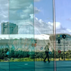 Fabienne · 28/03/2026 · 3601 x 3601 Cette photographie met en scène une réflexion dans une vitre moderne. Le sujet principal est la silhouette d’une personne marchant devant un bâtiment contemporain, visible à travers le verre. La composition joue sur les reflets et les superpositions, créant une ambiance presque symétrique.Le cadrage est serré sur la vitre, capturant aussi des éléments urbains en arrière-plan. La lumière est naturelle, avec des contrastes doux entre ombres et éclats. Les couleurs dominantes sont les teintes bleutées et grises du verre, avec des touches de vert et de blanc dans les reflets.Le style est épuré et contemporain, évoquant une ambiance urbaine et architecturale moderne.