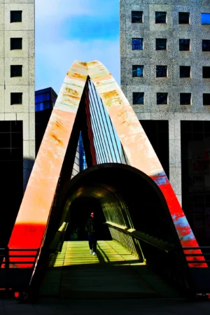 Fabienne · 28/03/2026 · 2357 x 3536 Cette photographie met en scène une sculpture architecturale géométrique en forme de V inversé, appelée "Les Voiles" (à São Paulo). Le sujet principal est cette structure métallique aux courbes élégantes, reflétant des couleurs vives.La composition joue sur les contrastes entre les lignes droites des bâtiments environnants et les courbes de la sculpture. Le cadrage serré isole la structure, accentuant son impact visuel. La lumière naturelle, probablement en fin de journée, crée des ombres marquées et des reflets colorés (rouge, jaune, bleu).Les couleurs dominantes sont les tons chauds (rouge, jaune) et froids (bleu), renforçant le dynamisme. Le style est moderne et architectural, évoquant une ambiance à la fois futuriste et artistique.