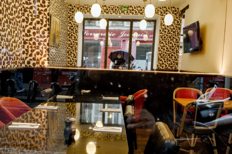 Frédéric · 11/04/2026 · 2517 x 1680 Cette photographie montre l'intérieur d'un café ou d'un salon aux accents exotiques. Le sujet principal est l’espace aménagé avec des fauteuils et des tables en bois, dont certains sont recouverts de peaux ou de tissus animaux.La composition est symétrique, avec un comptoir central et des chaises disposées de manière ordonnée. Le cadrage est serré, mettant en valeur les détails du mobilier et des murs ornés de motifs léopard.La lumière est douce et artificielle, créant une ambiance chaleureuse. Les couleurs dominantes sont les tons beiges, bruns et noirs, avec des touches de rouge et d’orange. Le style est bohème-chic, évoquant une ambiance cosy et élégante.