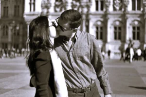 Fabienne · 04/04/2026 · 3393 x 2262 Cette photographie en noir et blanc met en scène un couple comme sujet principal, en train de s'embrasser. La composition est centrée sur eux, avec un cadrage serré qui isole leur intimité. L'arrière-plan, légèrement flou, montre une architecture classique et des passants, suggérant un lieu public.La lumière douce et naturelle accentue les contrastes sans être trop forte. Les tons dominants sont les gris et noirs, typiques du noir et blanc, avec quelques touches claires sur les visages et les vêtements.Le style est sobre et intemporel, évoquant une ambiance romantique et nostalgique.