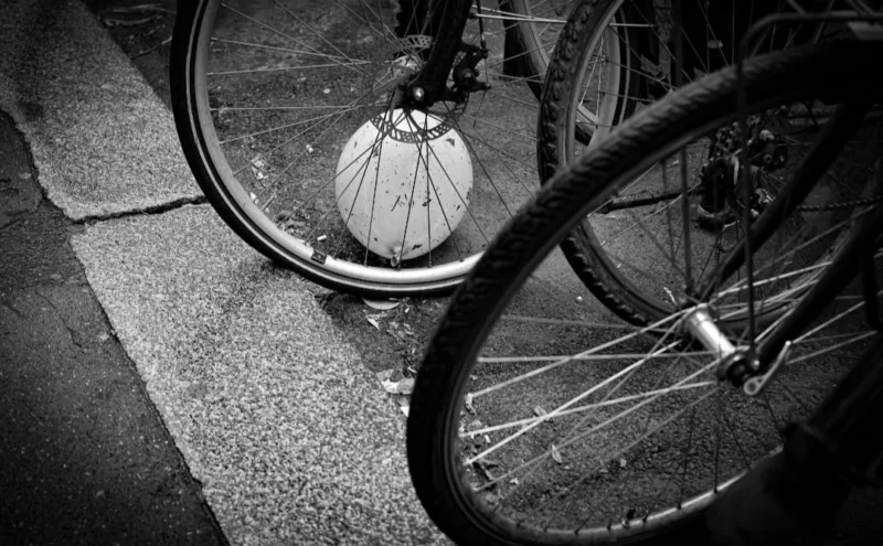 Muriel · 1080 x 668 Cette photographie met en scène deux roues de vélo comme sujet principal. La composition est centrée sur les roues, avec un cadrage serré et légèrement bas, créant un effet de profondeur et de perspective.La lumière, douce et contrastée, accentue les textures des pneus et des rayons. Les couleurs dominantes sont les tons de gris, typiques d’une image en noir et blanc, renforçant l’ambiance nostalgique et minimaliste.Le style est épuré et artistique, évoquant une atmosphère à la fois urbaine et intemporelle. L’ombre et la lumière ajoutent une touche dramatique, soulignant la simplicité et l’élégance du sujet.