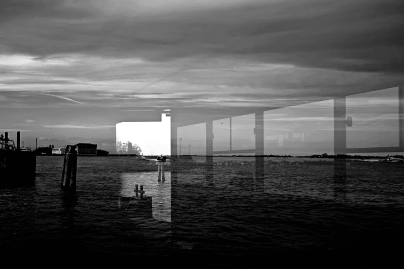 Fabienne · 09/04/2026 · 4566 x 3044 Cette photographie en noir et blanc met en scène un bâtiment moderne aux formes géométriques, partiellement reflété dans l’eau calme. Le sujet principal est ce bâtiment futuriste, dont les lignes épurées et les structures transparentes dominent la composition.Le cadrage est large, incluant un horizon bas et un ciel nuageux. La lumière, douce et diffuse, crée des contrastes subtils entre ombres et reflets. Les couleurs, limitées au noir, blanc et gris, renforcent l’aspect minimaliste et contemplatif. Le style est épuré et architectural, évoquant une ambiance à la fois sereine et mystérieuse.