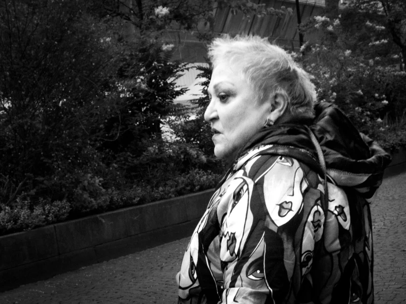 Muriel · 11/04/2026 · 2048 x 1463 Cette photographie met en scène une femme âgée comme sujet principal, vue de profil. La composition joue sur le flou d'arrière-plan, mettant en valeur son visage et ses traits expressifs. Le cadrage serré et légèrement bas accentue son regard et son expression mélancolique.La lumière est douce, créant des contrastes subtils. En noir et blanc, les tons varient du clair au foncé, renforçant les textures du vêtement et des cheveux.Le style est documentaire et intime, évoquant une ambiance contemplative et presque poétique.