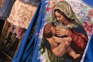 Muriel · 25/04/2026 · 2048 x 1365 Cette photographie met en scène une peinture religieuse représentant la Vierge à l'Enfant. Le sujet principal est Marie tenant l'Enfant Jésus.La composition montre un cadrage serré sur ce tableau, avec des éléments de draperies colorées en arrière-plan. La lumière semble douce et naturelle, mettant en valeur les détails et les textures. Les couleurs dominantes sont des tons chauds (rouges, bleus profonds, ocres) et des teintes pastel.Le style évoque une peinture traditionnelle, probablement inspirée de l'art byzantin ou de la Renaissance. L'ambiance est à la fois sacrée et intime, empreinte de sérénité et de dévotion.