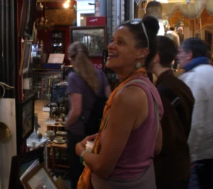 Bao · 3837 x 3396 Cette photographie montre une femme comme sujet principal, souriante et détendue, dans un lieu qui semble être un bar ou un magasin. Elle porte une tenue décontractée, rose, et ses bras sont croisés.La composition est dynamique, avec plusieurs personnes en arrière-plan légèrement floues. Le cadrage est serré sur la femme, mettant en valeur son expression joyeuse. La lumière est douce et tamisée, créant une ambiance chaleureuse et conviviale. Les couleurs dominantes sont des tons chauds (rose, brun, beige), renforçant l'atmosphère accueillante. Le style est réaliste et spontané, reflétant une scène de vie quotidienne.
