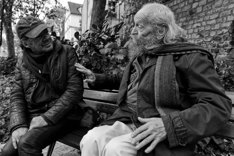 Mickaël · 11/11/2024 · 5009 x 3344 Cette photographie en noir et blanc met en scène deux hommes âgés assis sur un banc. Le sujet principal semble être l’échange entre eux, l’un souriant et l’autre plus pensif.La composition est simple et naturelle, avec un cadrage serré sur les deux personnages. La lumière douce, probablement naturelle, crée des contrastes doux et met en valeur les textures des vêtements et des visages.L’ambiance est intime et mélancolique, renforcée par le style documentaire et le choix du noir et blanc, évoquant une scène de vie quotidienne et authentique.