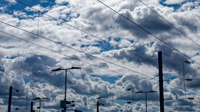 Bao · 2048 x 1152 Cette photographie met en scène des **lignes électriques et des poteaux** sous un ciel partiellement nuageux. Le **sujet principal** est l’architecture urbaine des infrastructures électriques, avec des fils de tramway et des câbles.La **composition** est épurée, avec un **cadrage serré** sur les éléments techniques, créant une perspective ascendante. La **lumière** naturelle, vive et contrastée, souligne les nuages et les ombres. Les **couleurs dominantes** sont les bleus et gris du ciel, avec des touches de blanc pour les nuages.Le style est **minimaliste et documentaire**, évoquant une **ambiance industrielle et moderne**, presque poétique par son jeu de lignes et de lumière.