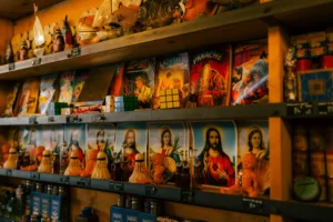Don · 25/04/2026 · 7008 x 4672 Cette photographie montre des étagères remplies de figurines et de boîtes de jeux ou de figurines de collection, probablement liées à des thèmes religieux ou historiques.La composition est serrée, avec un cadrage en plan rapproché mettant en valeur les détails des emballages. La lumière, douce et légèrement dorée, crée une ambiance chaleureuse et tamisée. Les couleurs dominantes sont des tons chauds : oranges, bruns et ocres, avec des touches de rouge et de bleu.L’ambiance est intimiste et nostalgique, évoquant un magasin spécialisé ou une boutique vintage. Le style est réaliste et photographié de manière à attirer l’attention sur les produits.