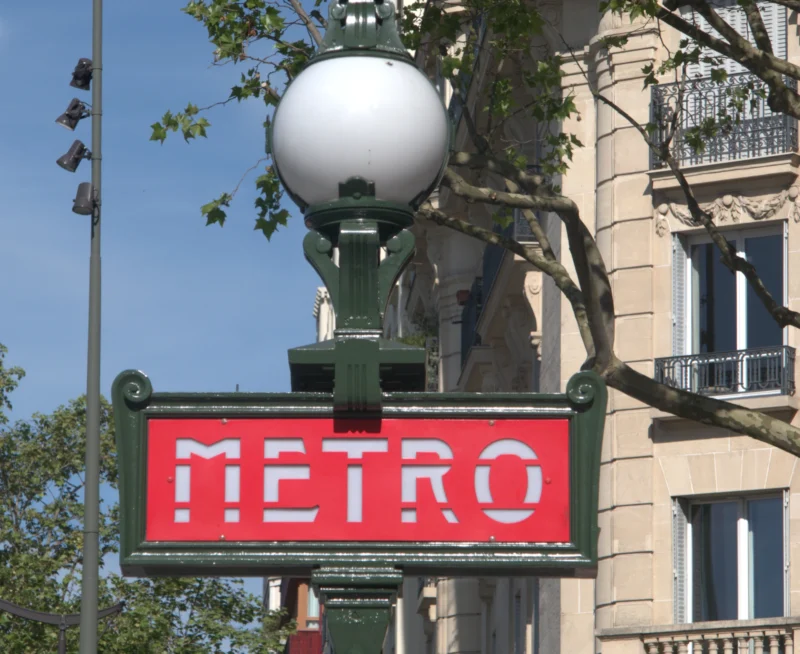 Bao · 4480 x 3664 Cette photographie met en scène un panneau "METRO" typique parisien, sujet principal identifiable par ses couleurs vives. La composition est centrée sur ce panneau, avec un cadrage serré qui isole partiellement l'élément. En arrière-plan, on aperçoit un immeuble haussmannien et une lampe à globe blanc.La lumière est naturelle, probablement diurne, avec des ombres douces. Les couleurs dominantes sont le rouge, le blanc et le vert du panneau, contrastant avec les tons beiges et verts des bâtiments. Le style est documentaire et urbain, évoquant une ambiance parisienne typique, à la fois dynamique et classique.