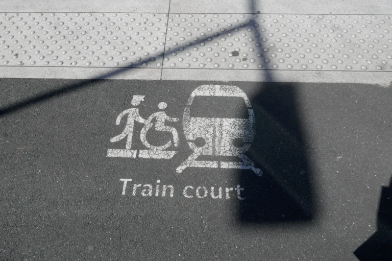 Bao · 23/04/2026 · 5472 x 3648 Cette photographie montre principalement un panneau indiquant un « Train court » avec des symboles de personnes en fauteuil roulant et de poussette. La composition est simple et épurée, avec un cadrage serré sur le panneau.La lumière naturelle crée une ombre nette, ajoutant un contraste. Les couleurs dominantes sont le gris (dominante) et le blanc des symboles. Le style est documentaire et fonctionnel, évoquant une ambiance pratique et accessible, typique des espaces publics dédiés aux transports.