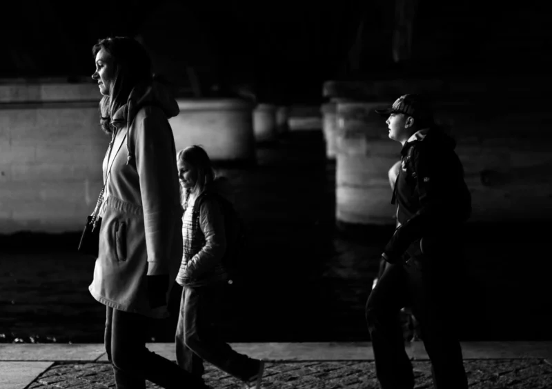 Bao · 2308 x 1628 Cette photographie en noir et blanc capture une scène nocturne urbaine. Le sujet principal semble être une femme en mouvement, vêtue d’un long manteau, au premier plan. La composition joue sur les contrastes entre les silhouettes et l’obscurité, créant une ambiance mystérieuse.Le cadrage serré et légèrement bas accentue le dynamisme des personnages. La lumière est faible, avec des jeux d’ombres et de clartés qui soulignent les contours. Les couleurs dominantes, bien que monochromes, exploitent les nuances de gris et de noir pour renforcer le côté dramatique.Le style est documentaire et réaliste, évoquant une ambiance mélancolique et introspective.