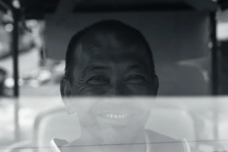 Don · 11/04/2026 · 5719 x 3813 Cette photographie met en scène un homme souriant, sujet principal, partiellement flouté. Le cadrage est serré sur son visage, avec un effet de flou artistique qui accentue son regard et sa bouche. La lumière est douce, sans contraste marqué, créant une ambiance tamisée. Les couleurs dominantes sont les tons gris et noirs, typiques d’un rendu monochrome ou sépia, renforçant une impression nostalgique ou intemporelle. Le style est épuré et minimaliste, évoquant une touche artistique et poétique, tout en instaurant une ambiance chaleureuse et humaine malgré le flou.