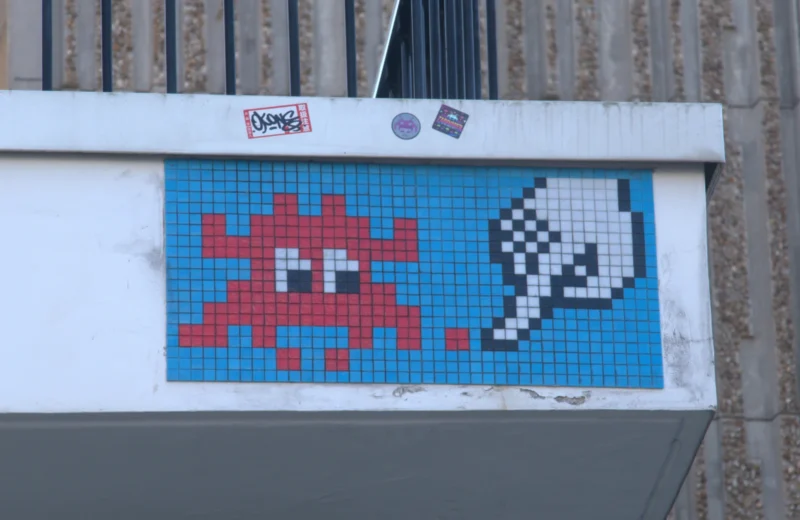 Bao · 5029 x 3270 Cette photographie montre un mural inspiré du jeu vidéo "Space Invaders". Le sujet principal est une mosaïque pixelisée représentant un alien rouge et un vaisseau spatial bleu.La composition est épurée, centrée sur ce motif rétro. Le cadrage est serré, mettant en valeur les détails des pixels. La lumière semble naturelle, sans ombre marquée, éclairant uniformément la surface.Les couleurs dominantes sont le bleu, le rouge et le blanc, typiques des jeux vidéo des années 80. Le style est minimaliste et nostalgique, évoquant une ambiance rétro et ludique.