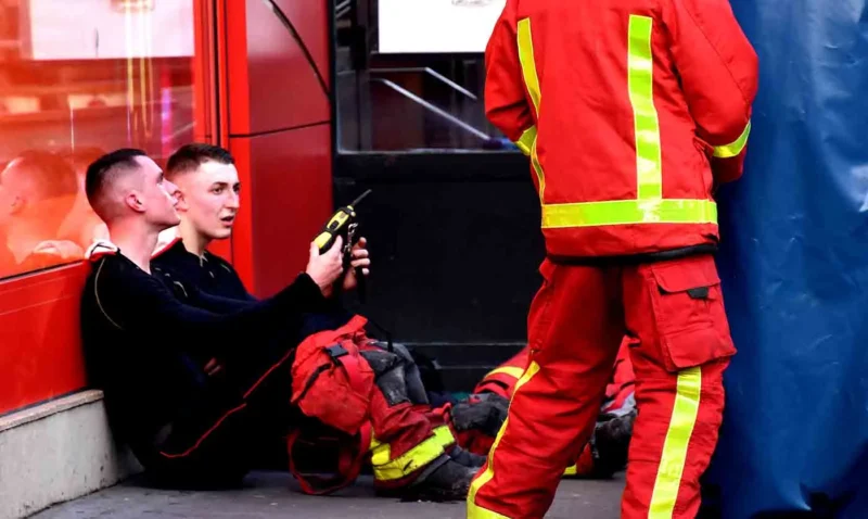 Franck T. · 12/03/2026 · 1400 x 837 Cette photographie montre deux pompiers en action. Le sujet principal est un jeune homme en uniforme noir, aidé par un pompier en tenue rouge et jaune, qui semble lui montrer une technique ou un équipement.La composition est dynamique, avec un cadrage serré sur les deux individus. La lumière est naturelle et semble provenir de l'extérieur, éclairant bien la scène. Les couleurs dominantes sont les tons rouges et noirs des tenues, avec des touches de bleu et gris en arrière-plan.Le style est réaliste et documentaire, capturant une situation professionnelle. L'ambiance est sérieuse et concentrée, reflétant l'urgence et la préparation des secours.