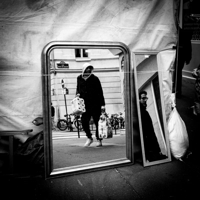 Jean-Philippe · 11/04/2026 · 4605 x 4605 Cette photographie en noir et blanc met en scène un homme comme sujet principal, reflété dans un miroir. La composition joue sur les reflets multiples, créant une impression de profondeur et de répétition.Le cadrage est serré sur le miroir, encadré par des tentures blanches. La lumière est douce, contrastant les ombres et les clartés, renforçant l'atmosphère mystérieuse. Les couleurs dominantes, bien que limitées au noir et blanc, accentuent les contrastes lumineux.Le style est artistique et contemplatif, évoquant une ambiance introspective et légèrement surréaliste.