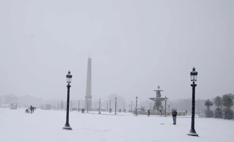 Franck T. · 06/01/2026 · 1400 x 852 Cette photographie capture un paysage hivernal enneigé. Le **sujet principal** est un **monument distant**, probablement un obélisque, partiellement dissimulé par le brouillard. La **composition** est symétrique, avec des **lampadaires alignés** au premier plan, créant une perspective menant vers l’horizon.Le **cadrage** est large, englobant une étendue plane et déserte. La **lumière** est faible, diffuse, atténuée par la neige et le ciel grisâtre. Les **couleurs dominantes** sont les tons froids : blanc de la neige, gris du ciel et noir des lampadaires.Le **style** est réaliste et sobre, évoquant une **ambiance mélancolique et paisible**, presque onirique.